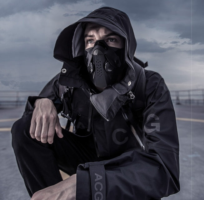 Person wearing a black hooded jacket and mask in an industrial setting