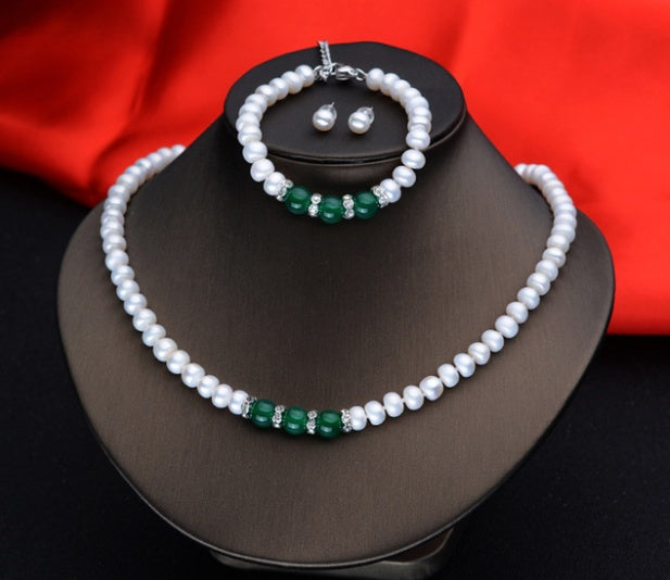 Pearl necklace with green accents and matching bracelet on a mannequin bust against a red fabric background.