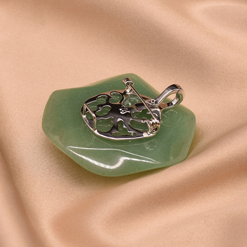 Silver pendant with a design on a green stone against a beige fabric background