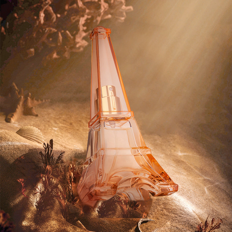 Perfume bottle shaped like the Eiffel Tower on a textured surface with a warm glow