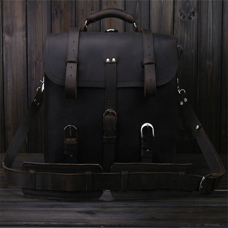 Dark leather satchel bag with multiple straps on a wooden surface