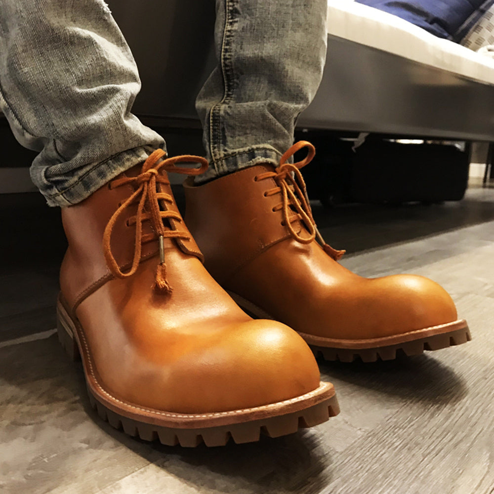 Brown leather boots with orange laces worn with jeans on a wooden floor.