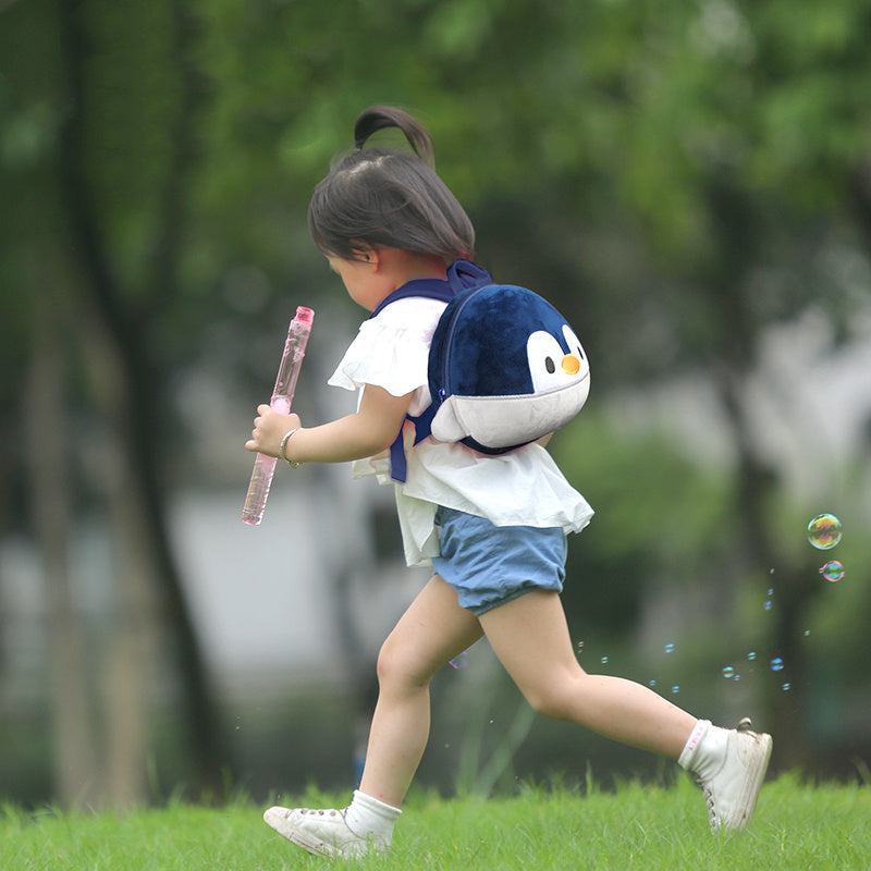 Child running outdoors with a penguin backpack and bubble wand