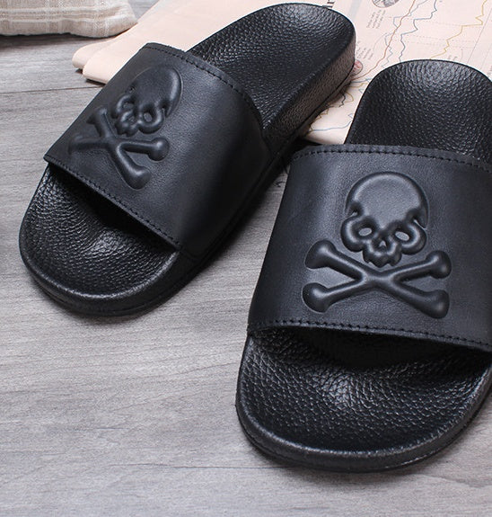 Black slides with skull and crossbones design on a wooden floor.