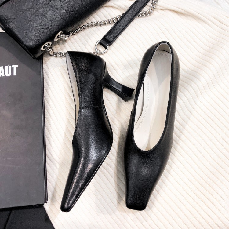 Black high-heeled shoes on a textured white surface with a black handbag and book.