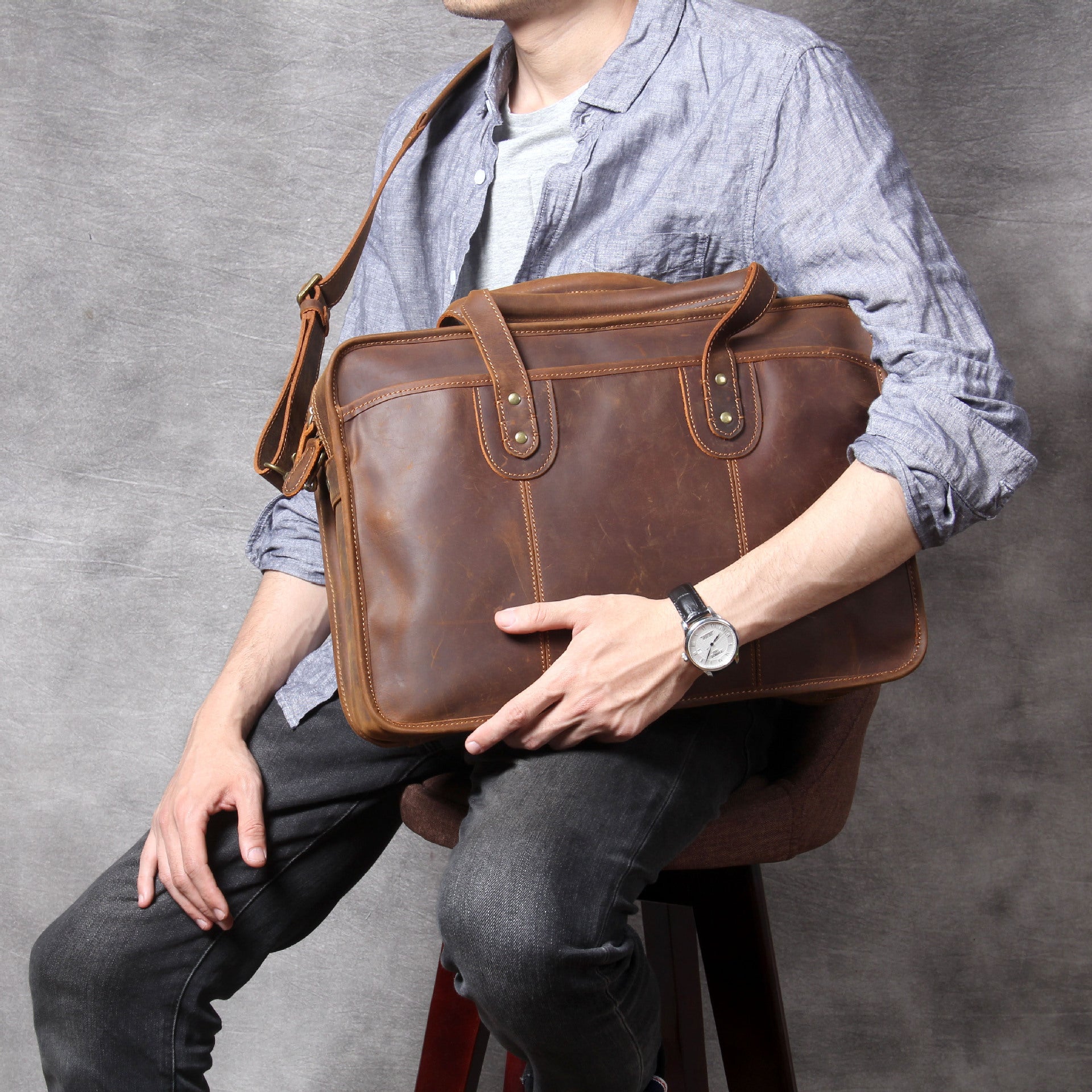 Person holding a brown leather bag against a gray background