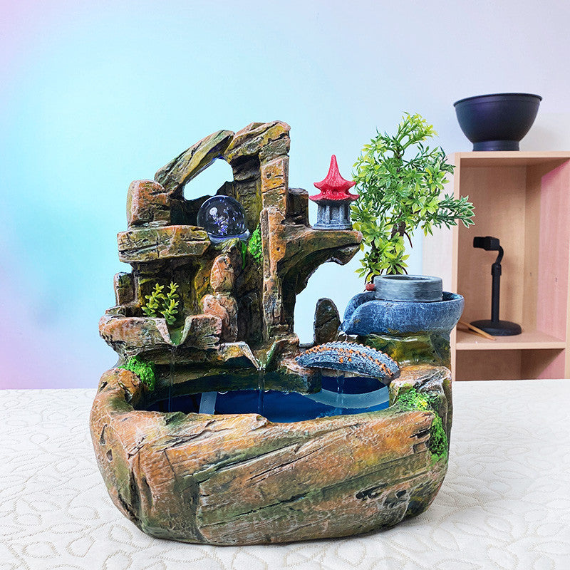 Decorative indoor water fountain with rocks, plants, and small structures on a light background