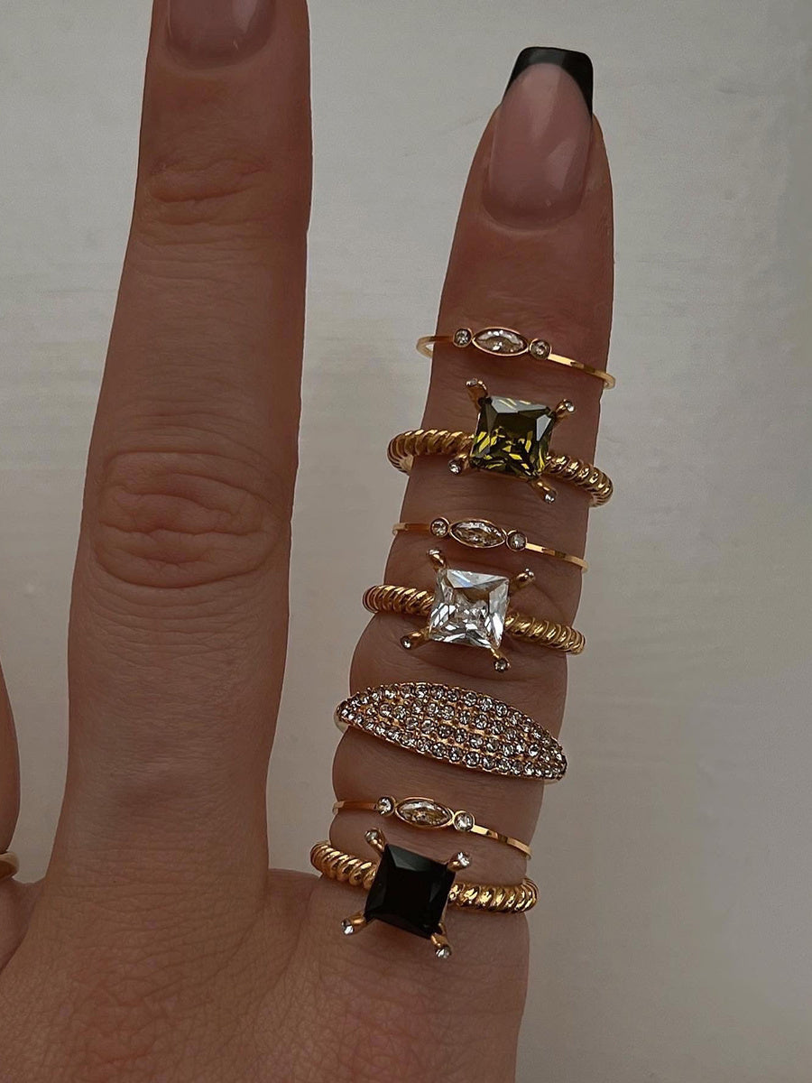 Multiple gold rings with various designs on a finger against a neutral background
