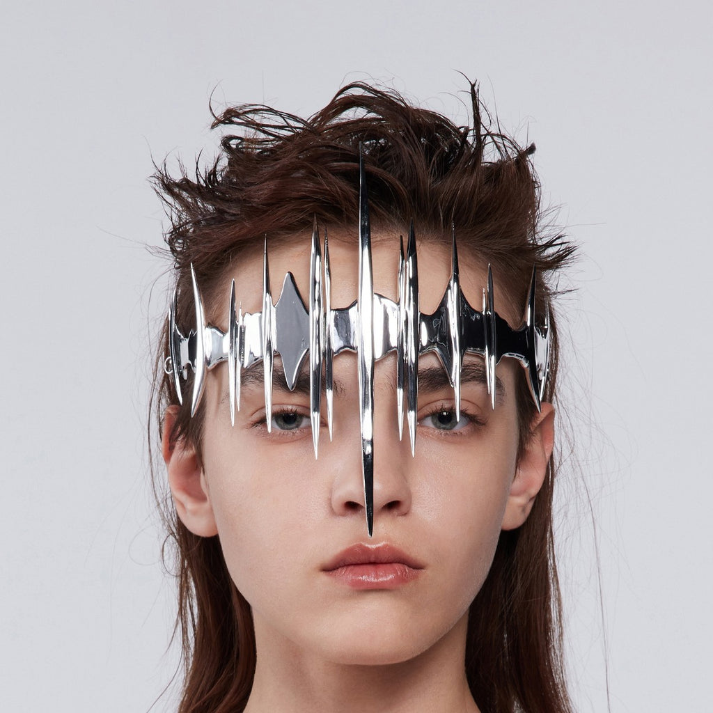 Person wearing a metallic face mask with geometric design on a plain background