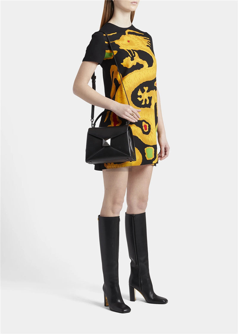 Woman wearing a black and yellow patterned dress with knee-high black boots on a white background