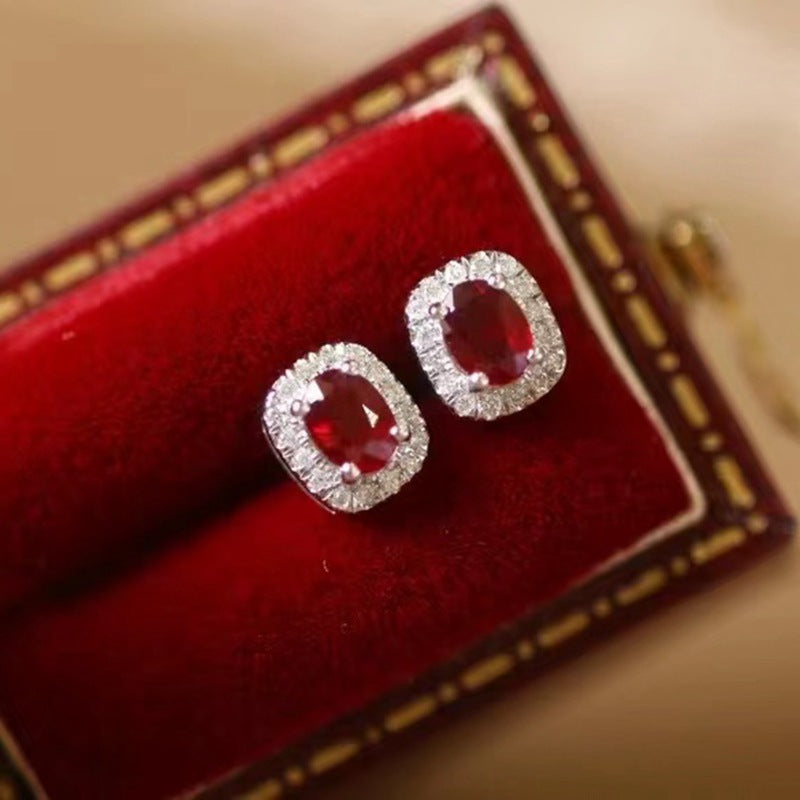 Pair of red gemstone earrings with silver frames on a red cushioned jewelry box.