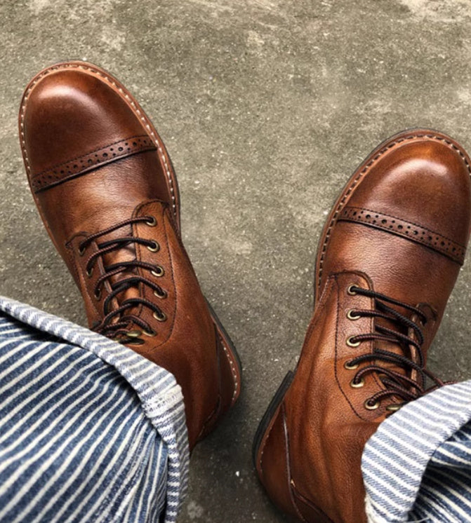 Brown leather shoes worn with striped pants on a concrete floor