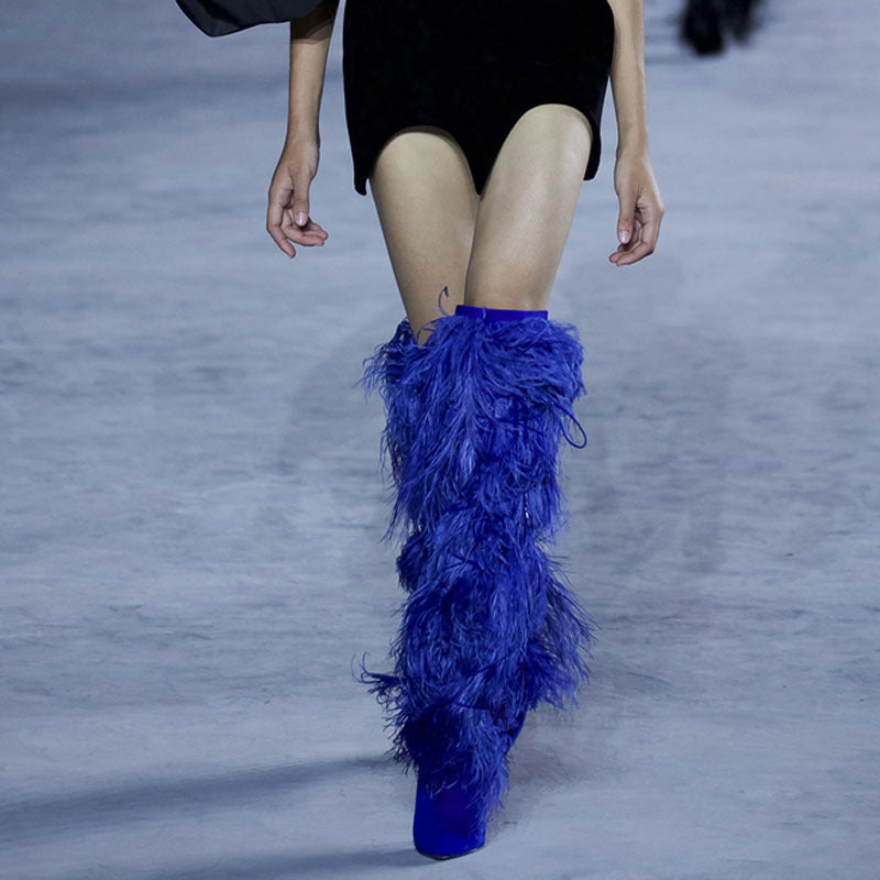 Blue feathered boots worn by a model on a runway.