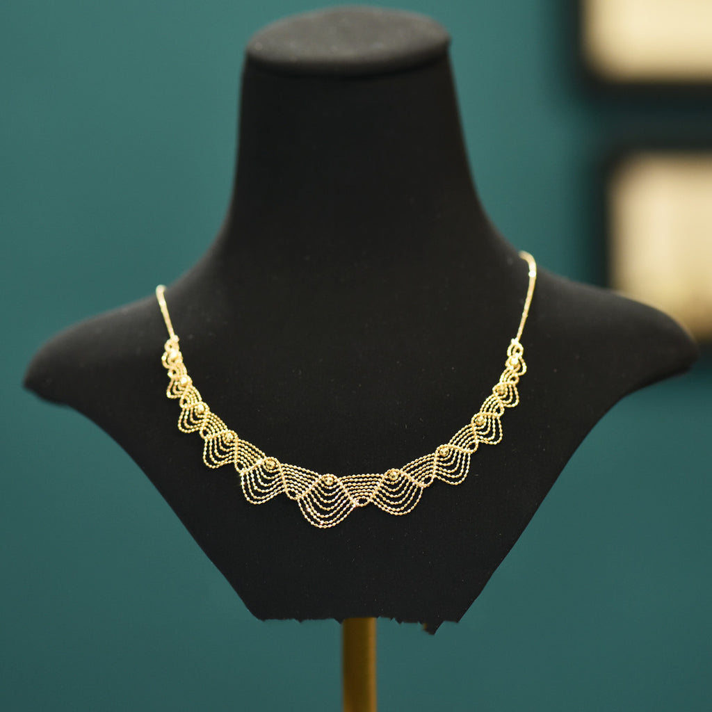 Gold necklace on a black mannequin bust against a teal background