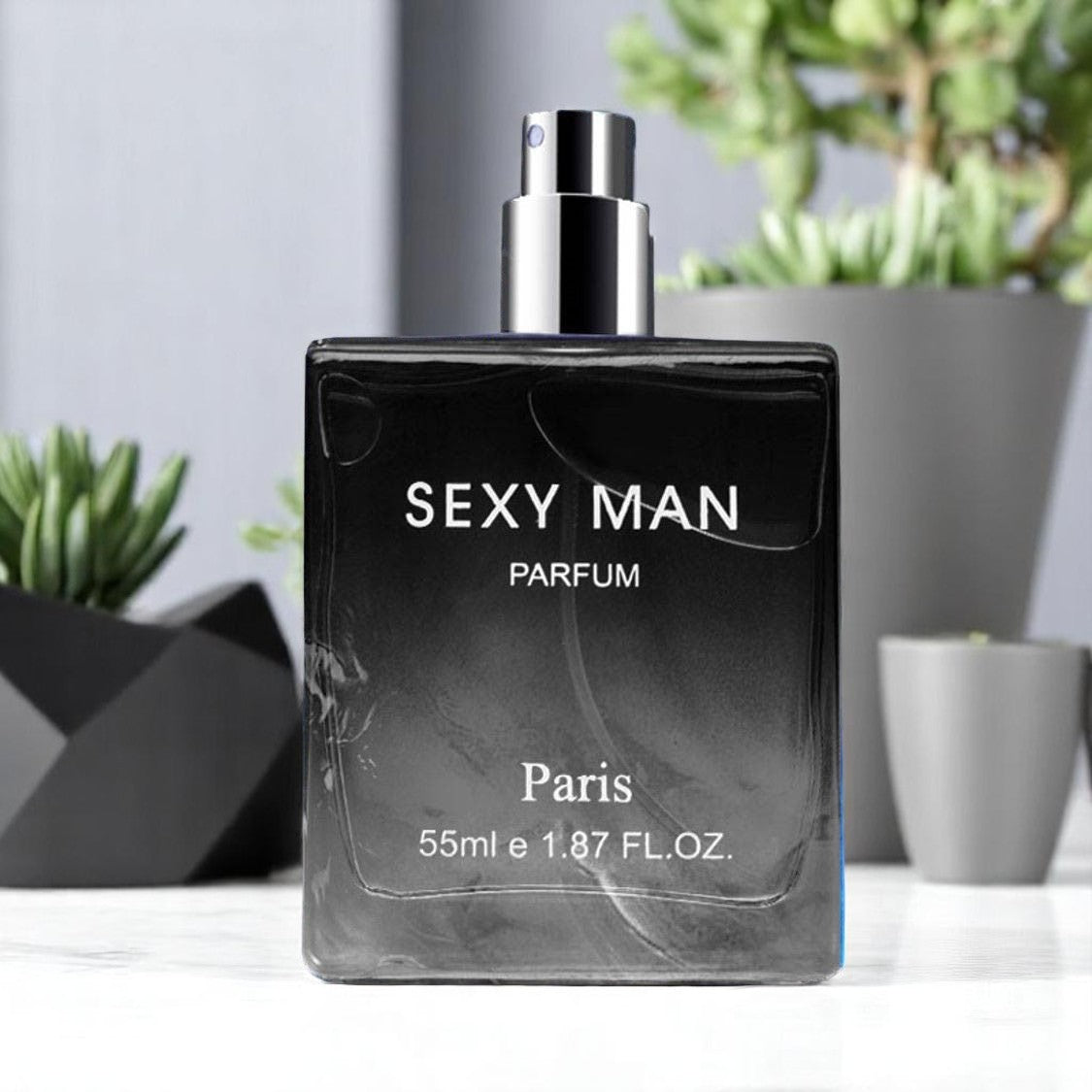 Black 'SEXY MAN PARFUM' bottle with silver cap on a white surface with plants in the background