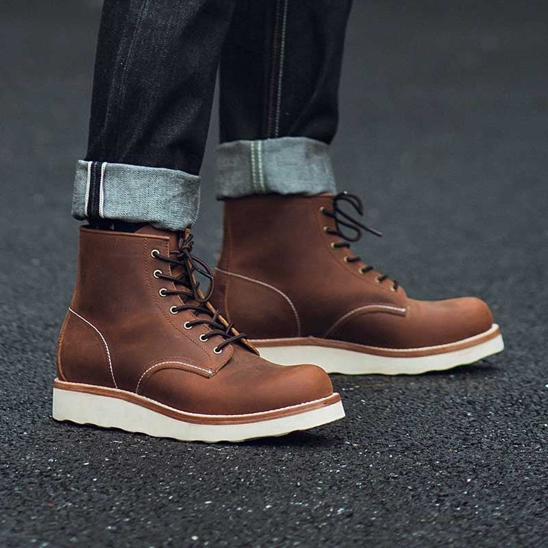 Brown leather boots with white soles worn with rolled-up jeans on a dark surface