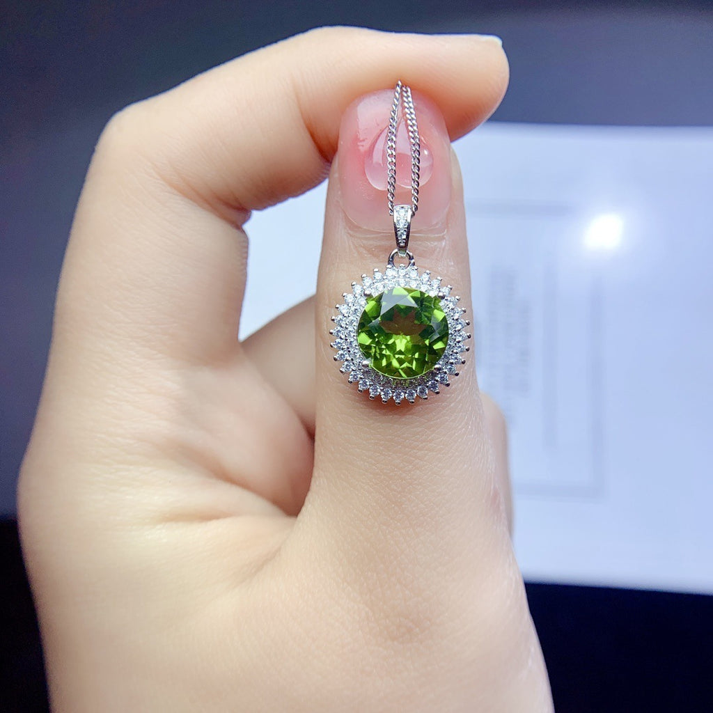 Hand holding a silver pendant with a green gemstone against a blurred background