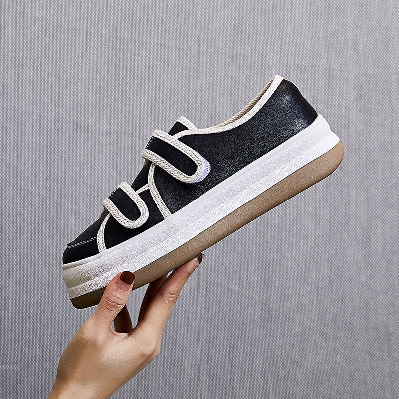 Black sneaker with white sole held by a hand against a gray background