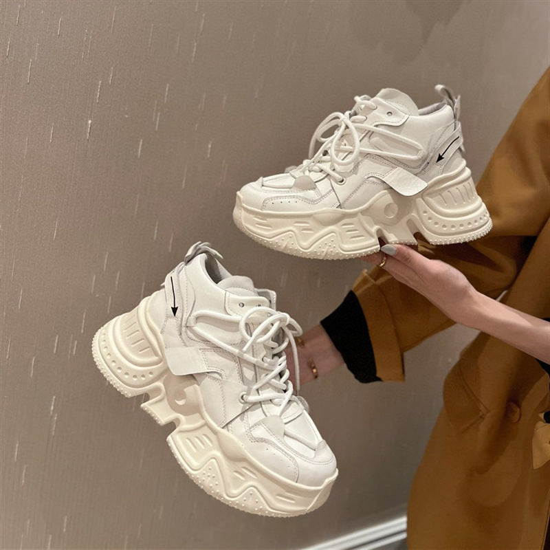 White sneakers held by a person wearing a mustard yellow coat against a brown background