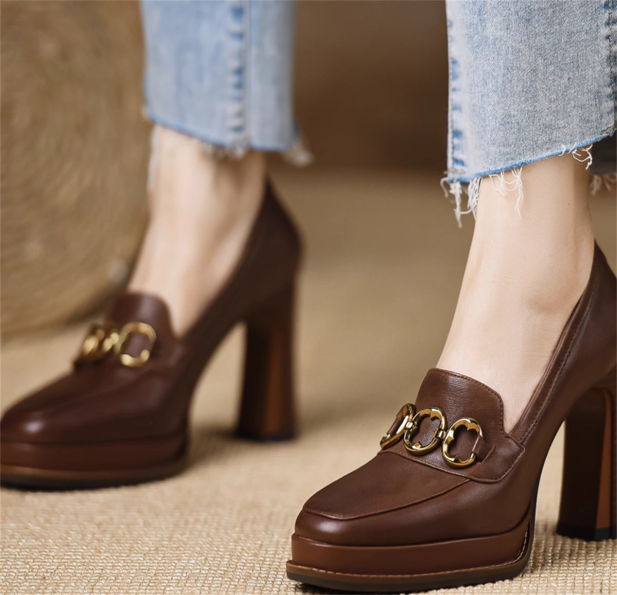 Brown high-heeled shoes with gold chain details worn with light blue jeans.