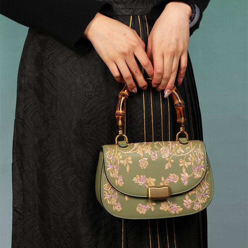 Green floral handbag with gold accents held by a person wearing a black dress.