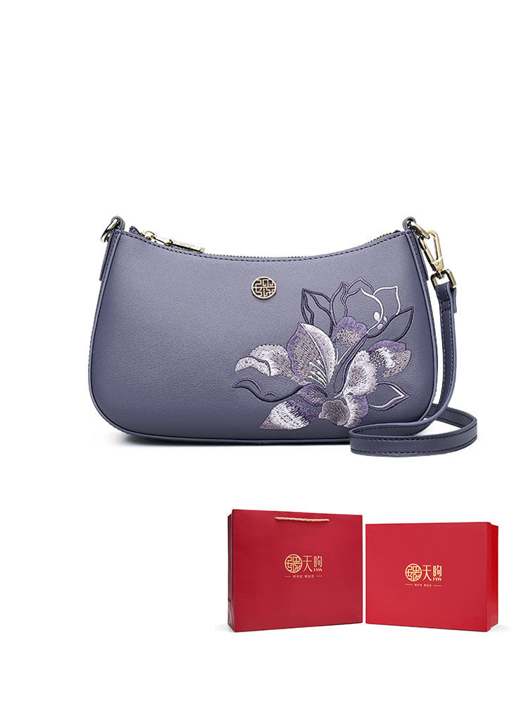 Purple handbag with floral embroidery and matching red box on a white background