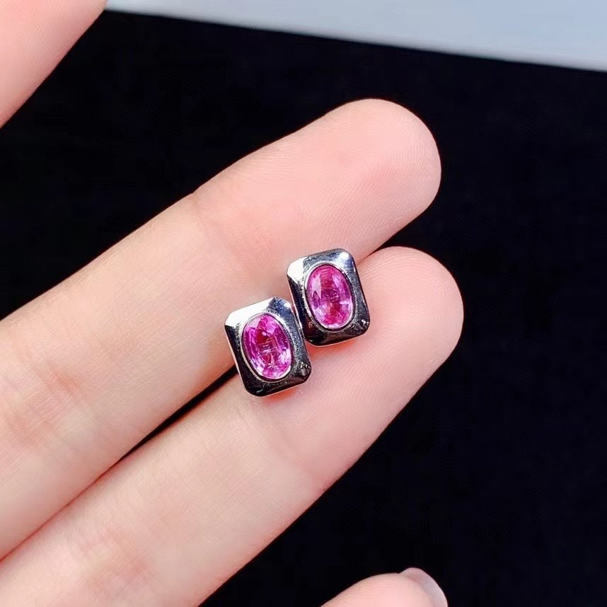 Pink gemstone stud earrings on a hand against a black background