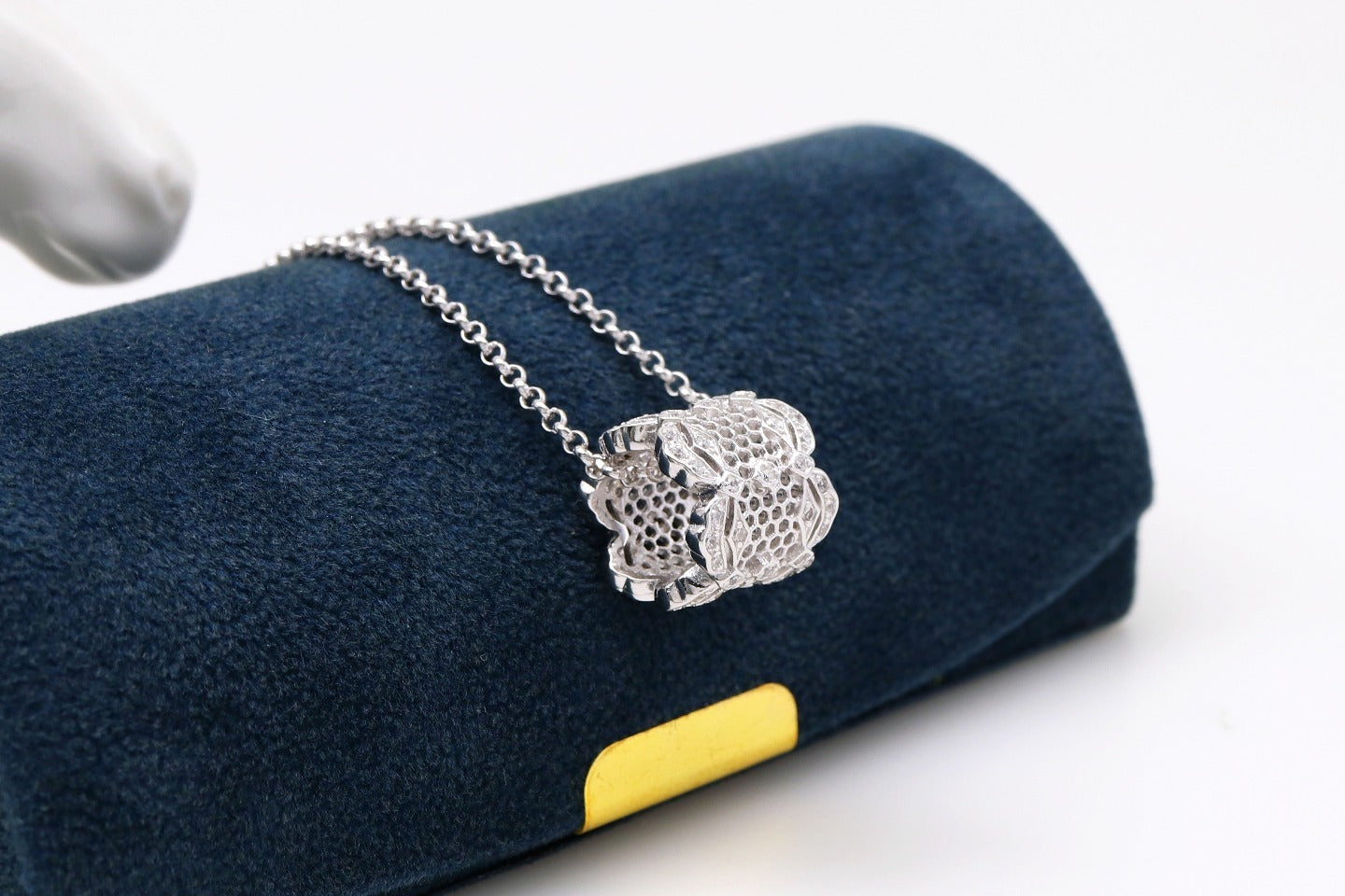 Silver necklace with a detailed pendant on a blue cushion with a yellow edge.