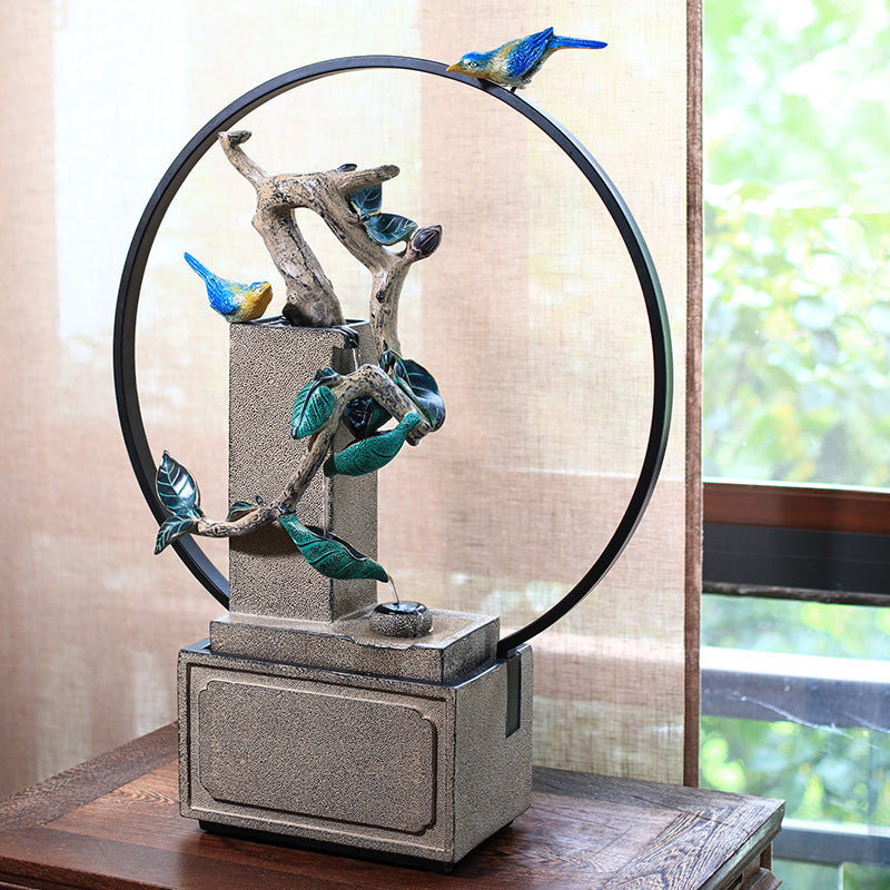Decorative fountain with birds on a branch in a circular frame.