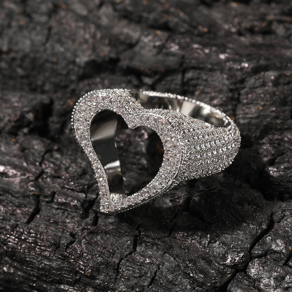 Silver heart-shaped ring with embedded stones on a dark textured surface