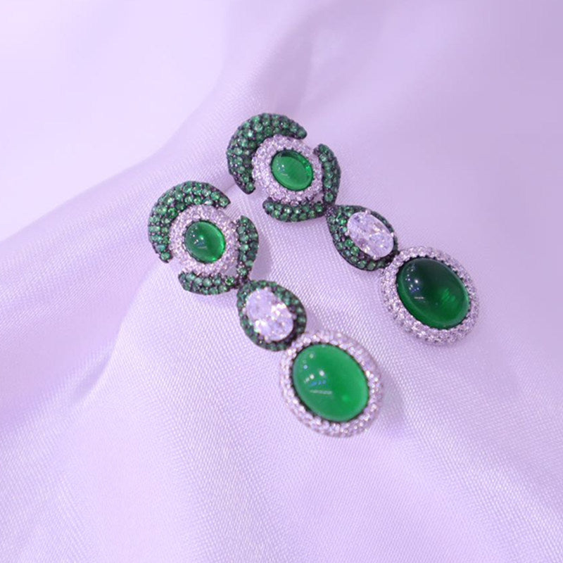 Green gemstone earrings on a light purple fabric background