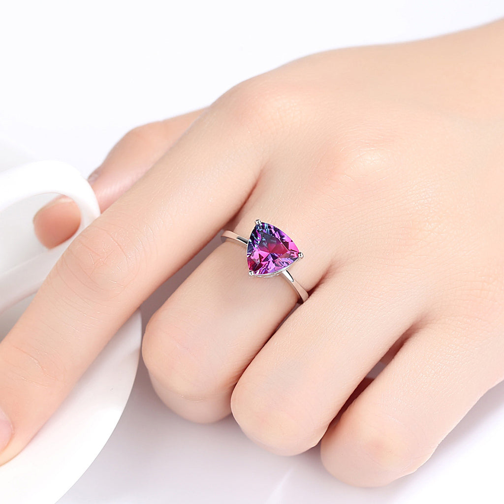 Hand wearing a ring with a heart-shaped purple gemstone on a white background