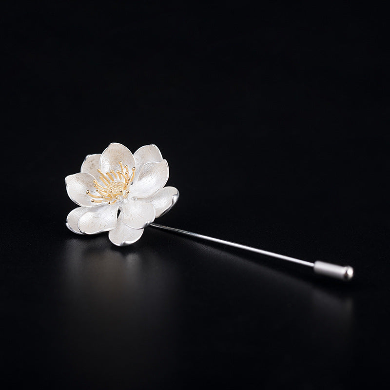 Floral brooch with white flower and gold center on a black background
