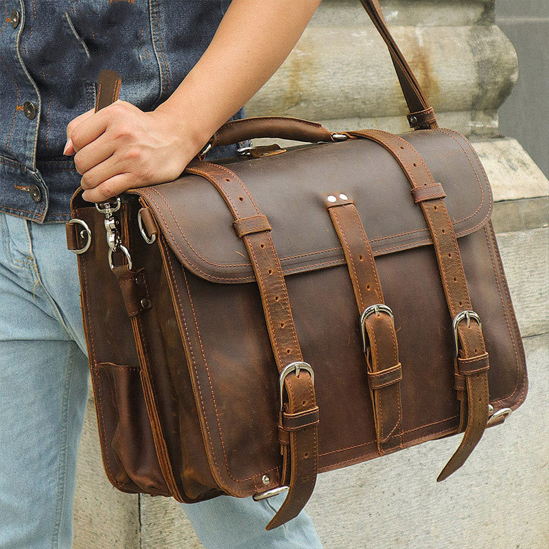 Brown leather satchel bag held by a person wearing a denim jacket and jeans.