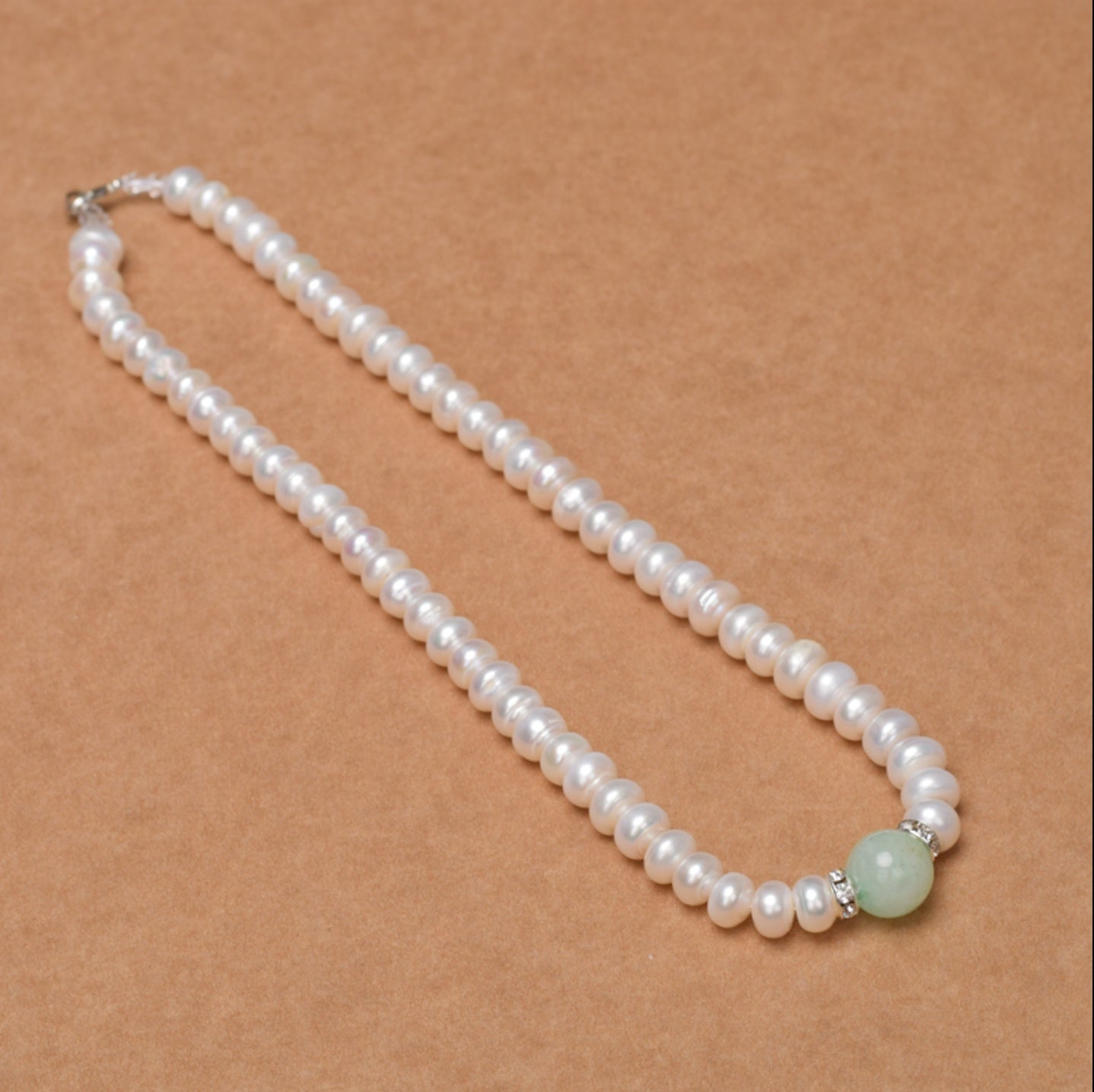 Pearl necklace with a green bead on a brown background