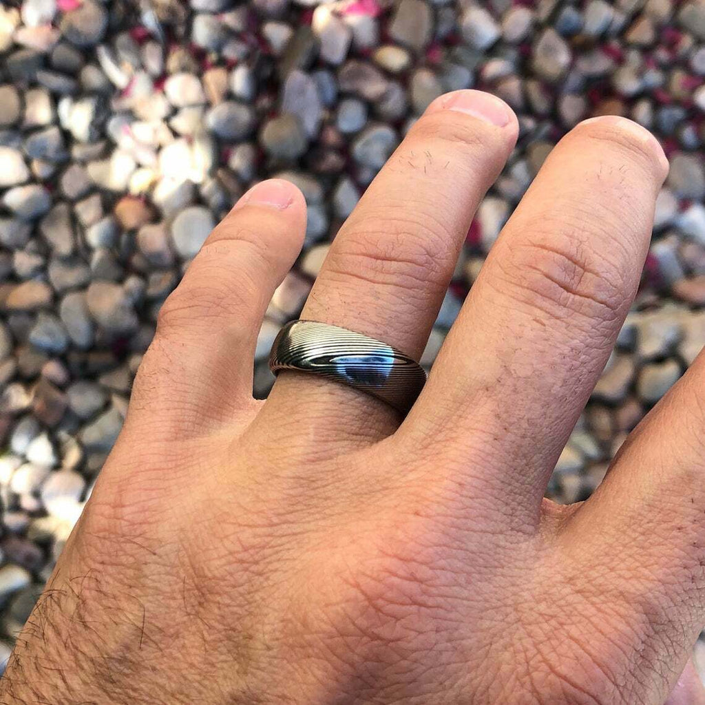 Hand wearing a ring with a textured band against a mosaic background