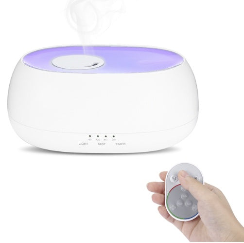 White humidifier with purple light on a white background, held by a hand with a remote control.