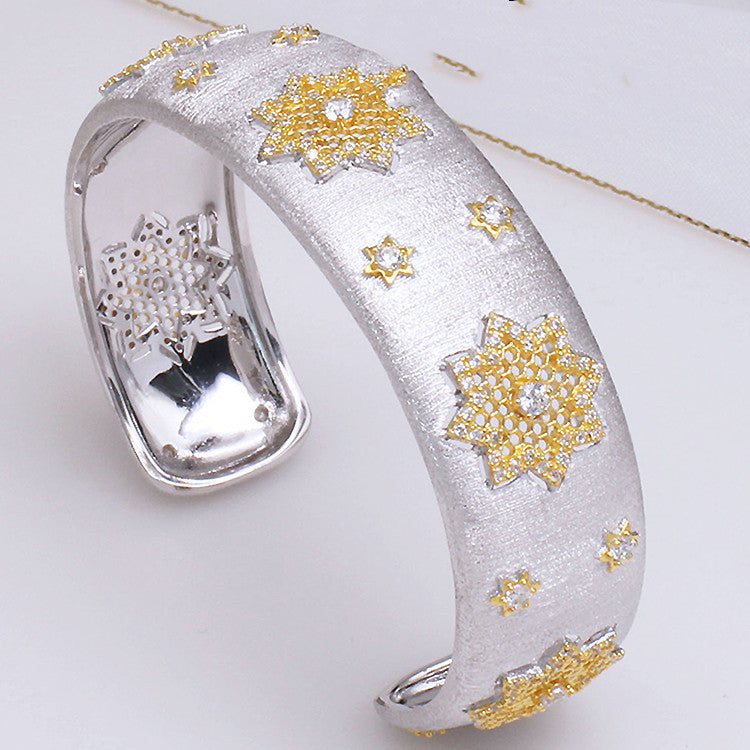 Silver bracelet with gold snowflake designs on a white background