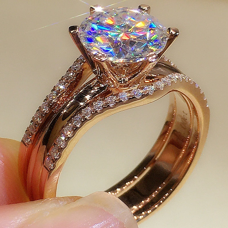 Rose gold ring with a large diamond and smaller diamonds on the band, held by a hand.