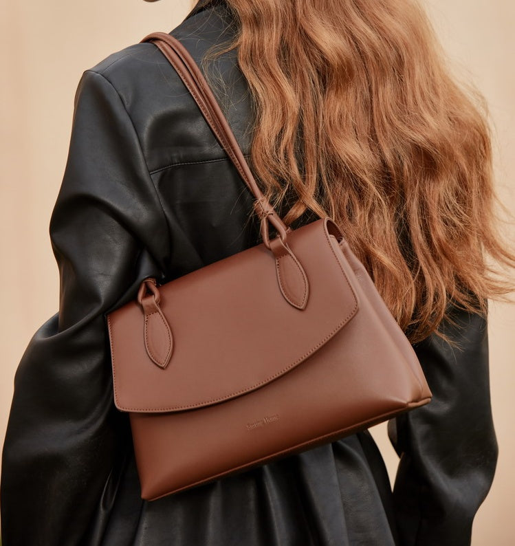 Brown leather handbag worn over shoulder against a neutral background