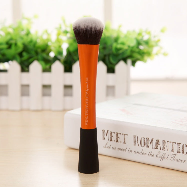 Makeup brush with orange handle and black ferrule on a surface with a blurred background