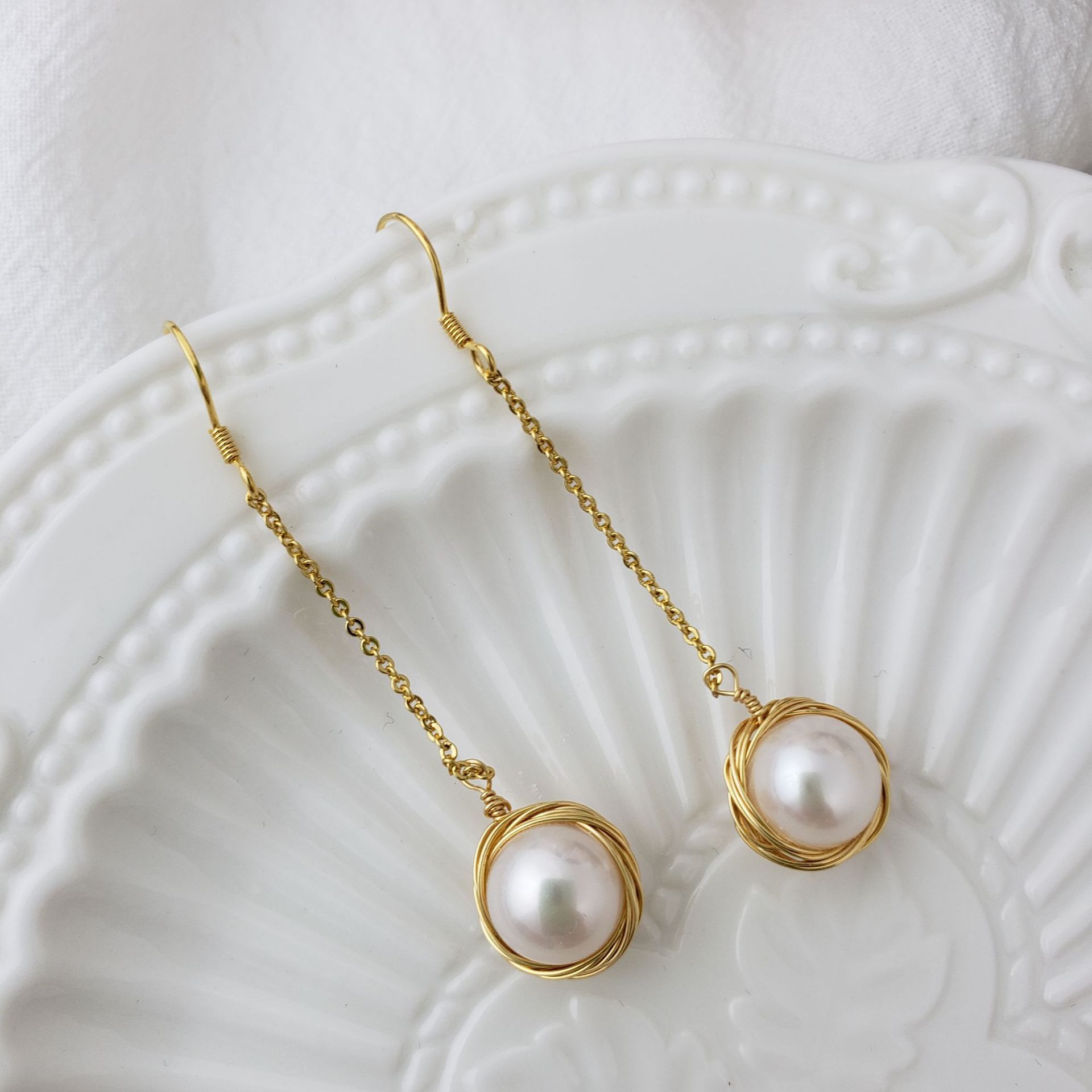 Gold earrings with pearl drops on a textured white surface