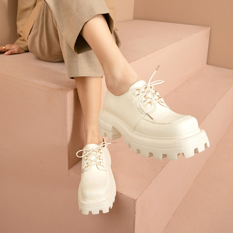 White platform shoes worn by a person sitting on a pink surface