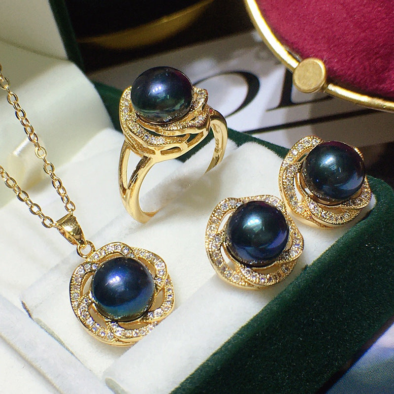 Jewelry set with gold rings and earrings featuring dark blue pearls on a white surface.