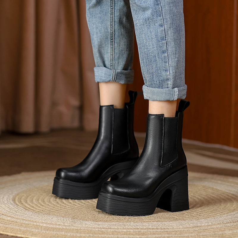 Black platform boots worn with rolled-up jeans on a neutral background