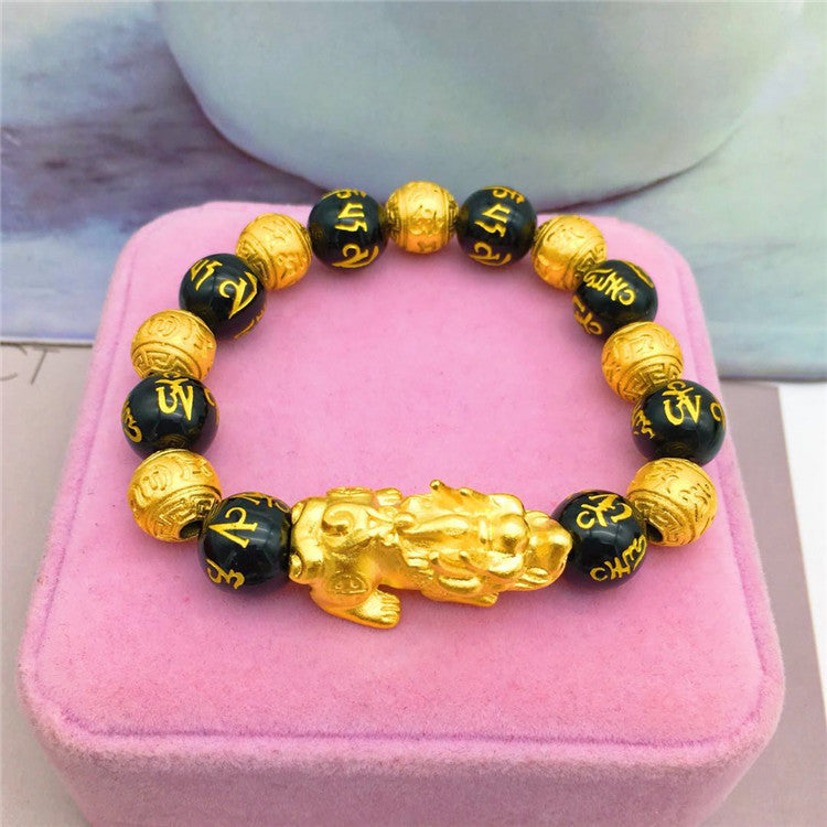 Black and gold beaded bracelet with a golden lion figure on a pink cushion