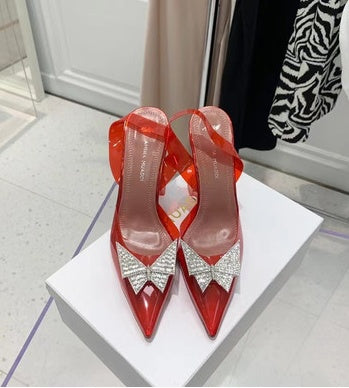 Red high-heeled shoes with crystal details on a white platform.