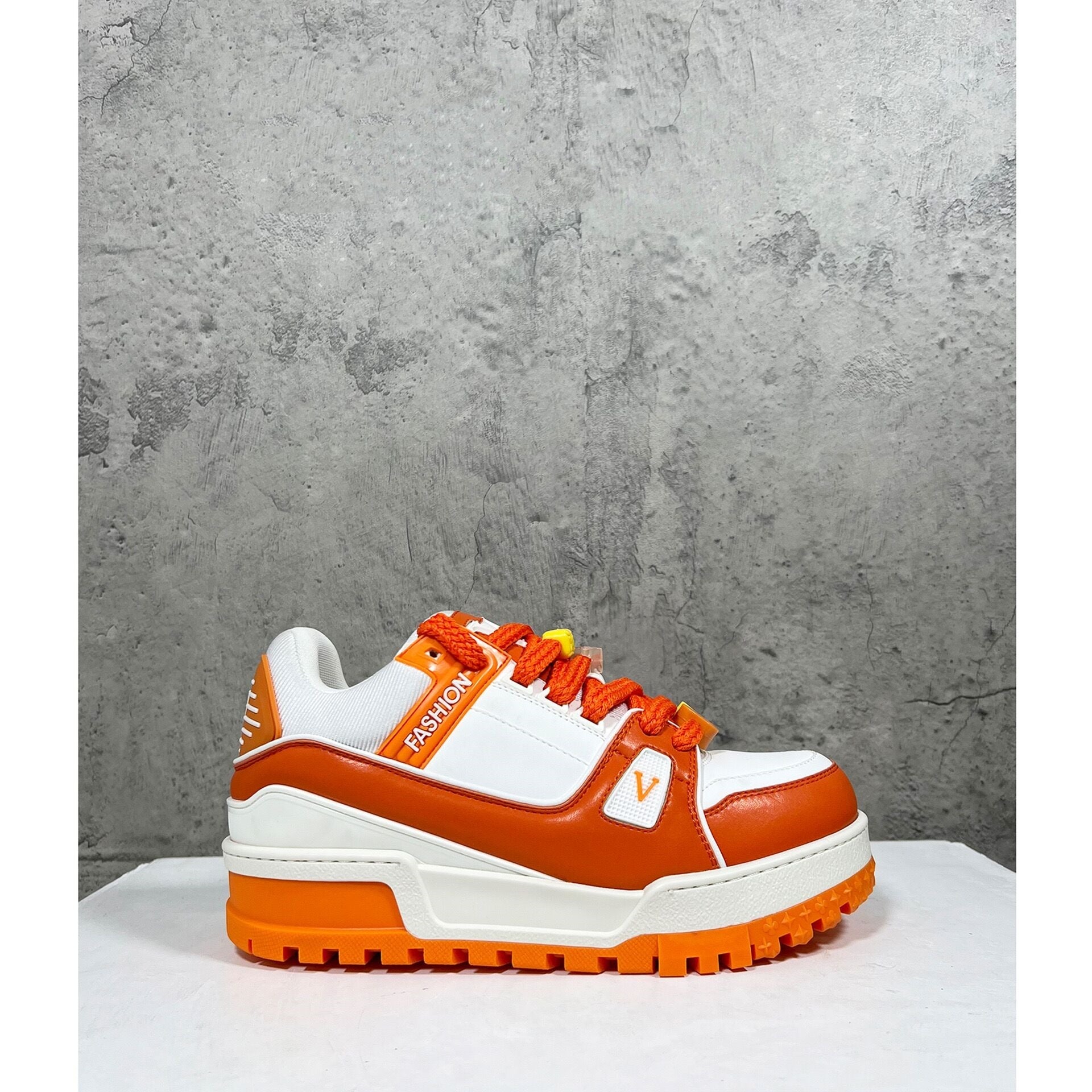 Orange and white sneaker with 'Fashion' branding on a gray concrete background