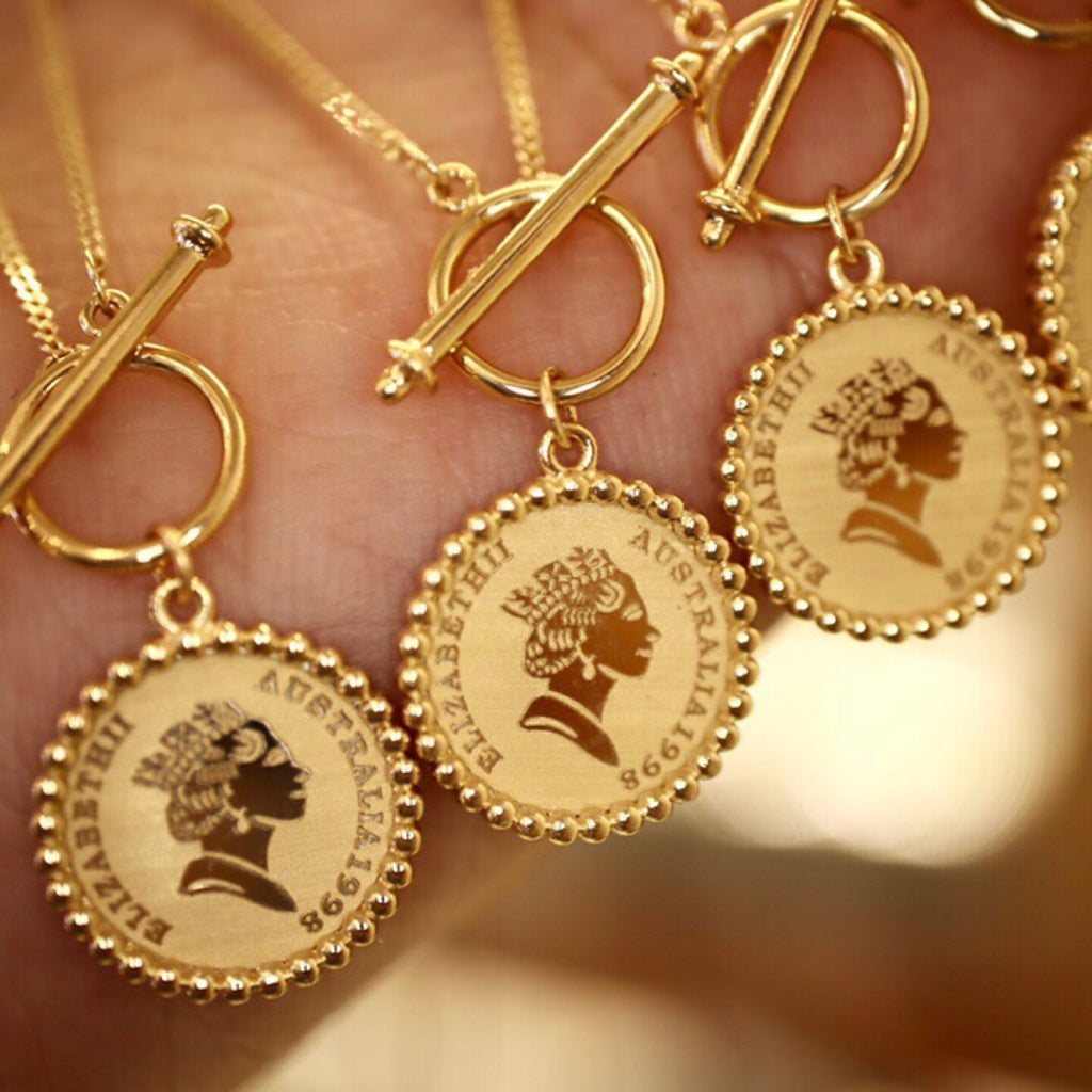 Gold necklaces with coin-style pendants featuring engraved faces on a blurred background.