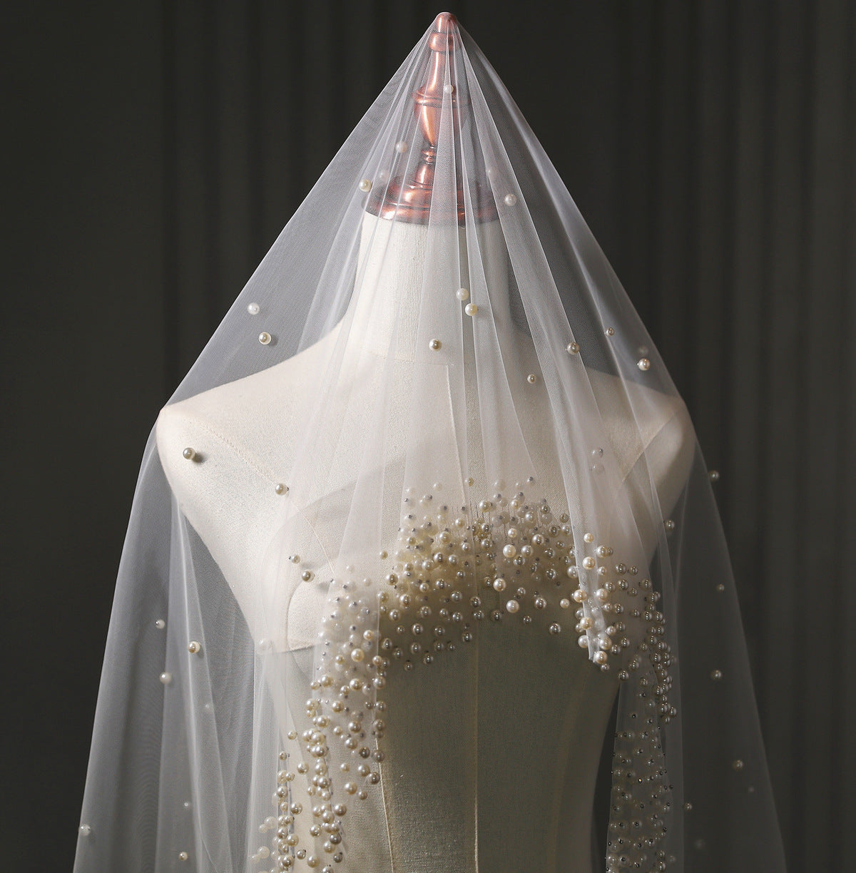 White wedding veil with pearl embellishments on a mannequin against a dark background